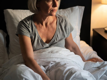Perimenopausal woman in her 40s sitting up in bed at night with restless legs syndrome, subtle discomfort, warm bedroom lighting - from Vibrance Way