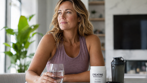 Realistic photo of a confident perimenopausal woman in her 40s sitting at a modern kitchen table with creatine monohydrate, a shaker bottle, and a glass of water, representing wellness, brain health, muscle support, and healthy aging during perimenopause.