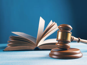 Livro aberto e martelo de juiz sobre superfície azul, fundo azul. Atmosfera de justiça e conhecimento jurídico.