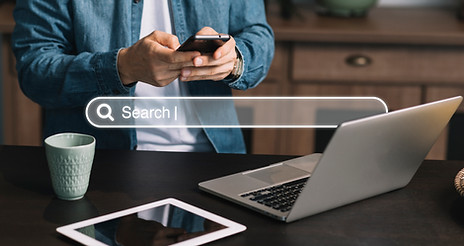 Person using smartphone near laptop with search bar overlay
