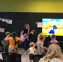 Woman singing and playing guitar for kids watching with dinosaur cartoon.