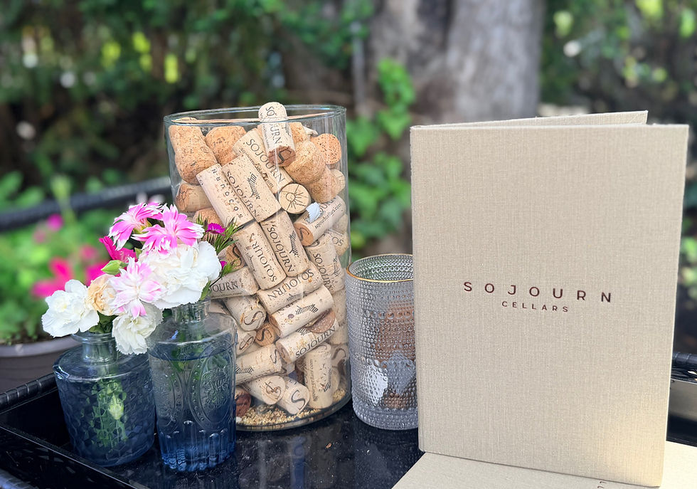 Glass vase with pink flowers beside a jar filled with wine corks and a Sojourn Cellars wine bag, creating a welcoming Wine Country display.