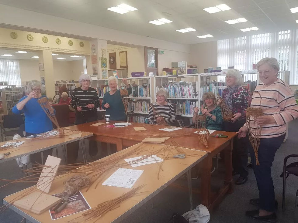 a group of people are sitting around a table in a library making baskets