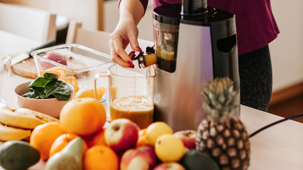 Person juicing fresh fruits and spinach in a kitchen. Vibrant fruits like oranges, apples, and a pineapple are on the counter. Warm setting.