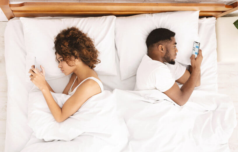 Black couple laying in bed on phones