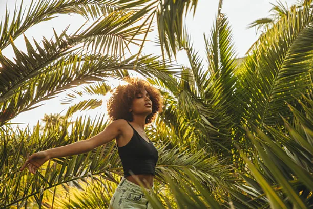 African American woman walking through palm tree leaves at peace