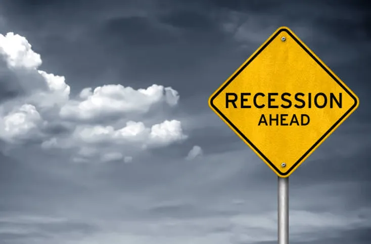Dark cloudy skies backgound with yellow traffic sign that states "Recession Ahead"
