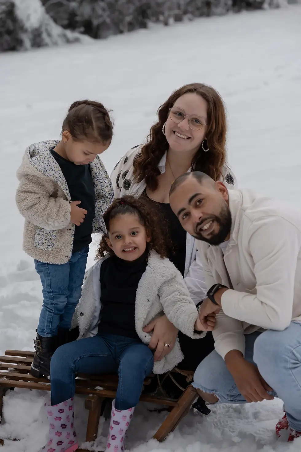 Famille souriante de quatre personnes posant joyeusement dans la neige hivernale.