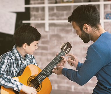 Boy and instructor playing guitar. Music lesson with brick wall in background.