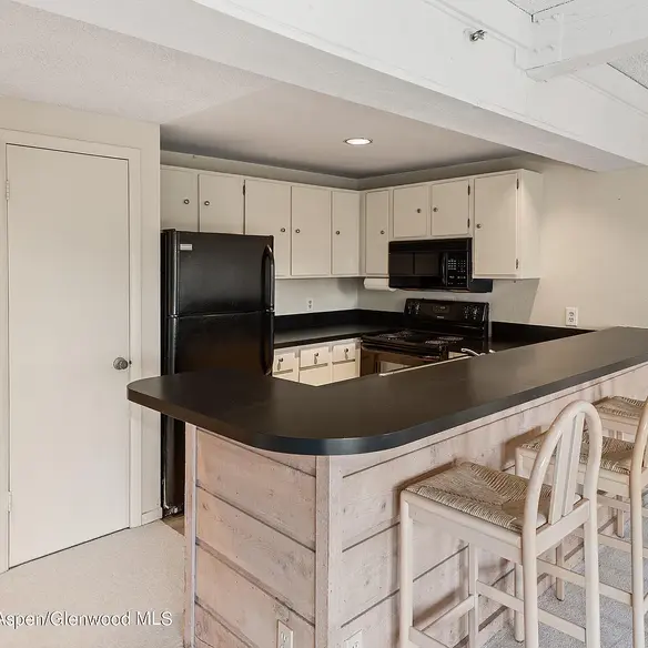 Before renovation photo of the kitchen with black appliances, laminate countertops, and white cabinets in the Snowmass Village condo.