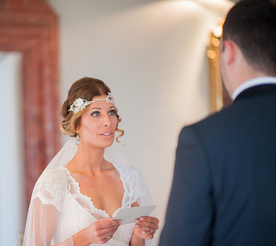 Die Braut trägt ein Headpiece im Vintage-Stil und liest ihr Ehegelübde – ein persönlicher Moment voller Emotionen.