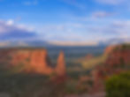 Red rock formations and cliffs under a bright blue sky with scattered clouds in a vast desert landscape, creating a serene and majestic view.