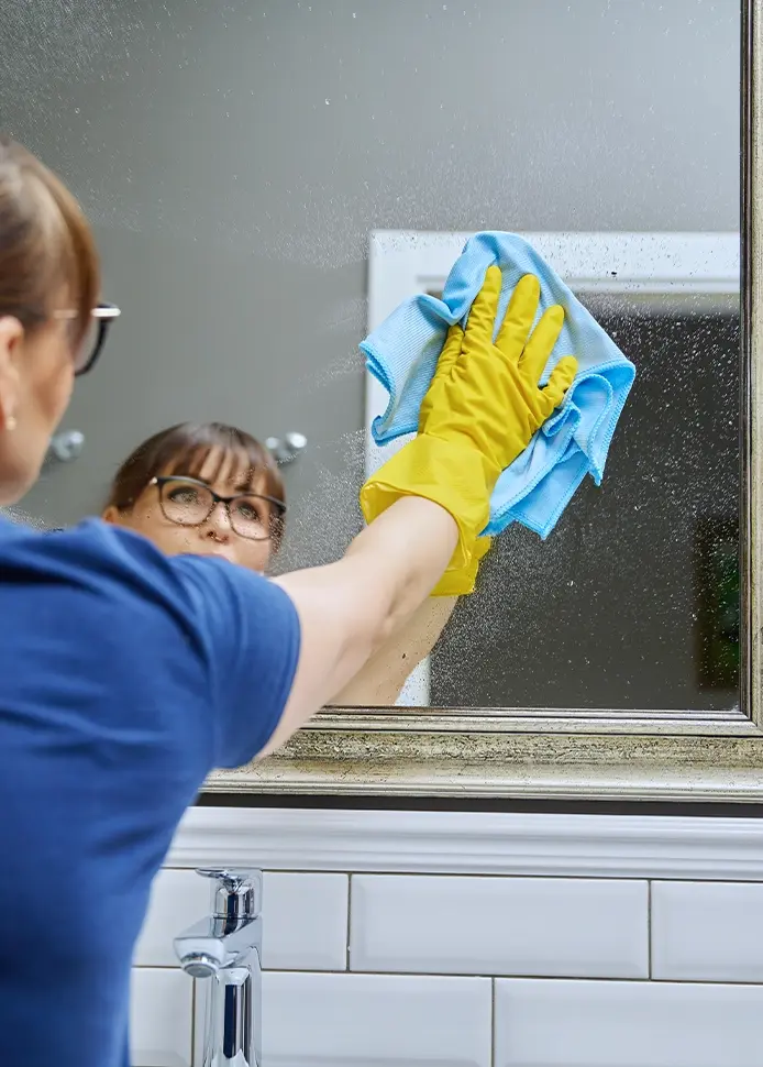 Maid cleaning bathroom mirror with microfiber cloth