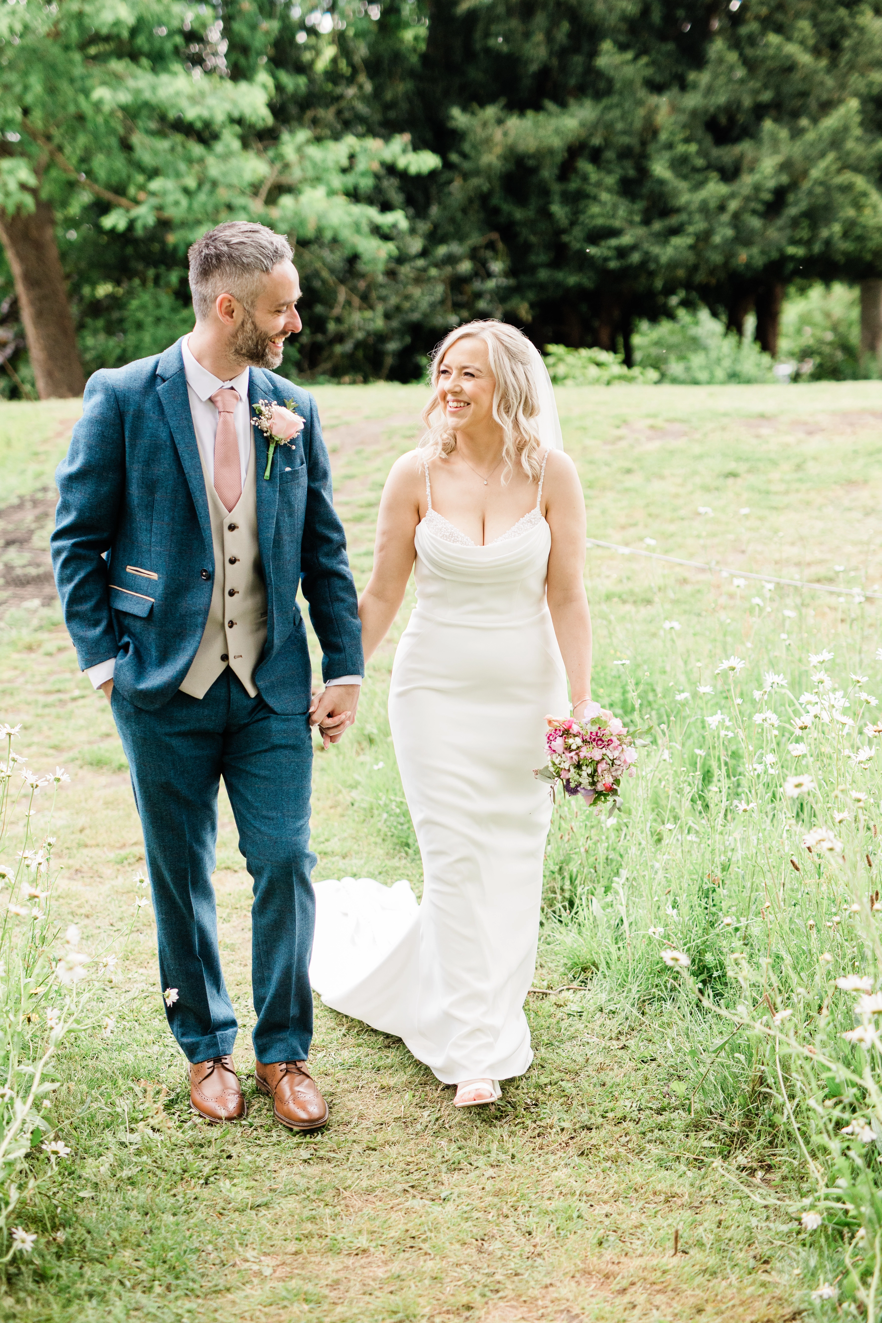 bride and groom walking through a field within the grounds of their wedding venue