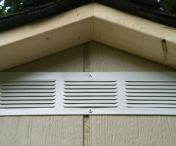 A close-up of a silver gable vent installed on a light-colored shed.