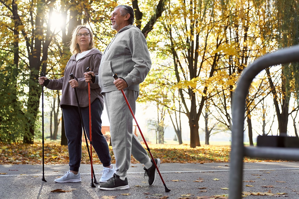 A couple in casual clothes is Nordic walking in a sunny park with autumn leaves. They appear content and engaged in conversation.
