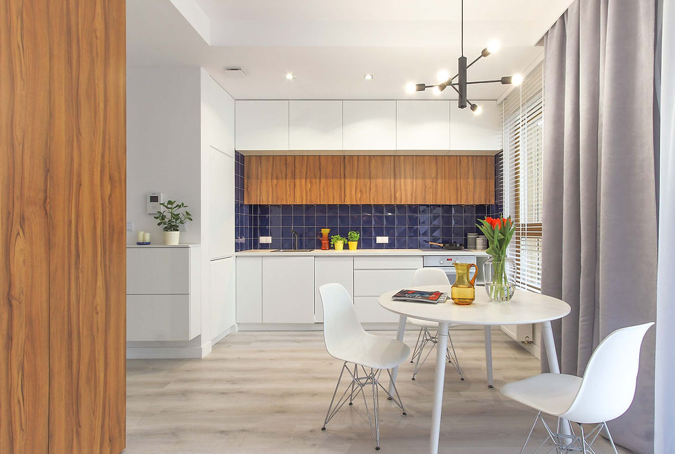 Okrągły stół z krzesłami na tle białej kuchni z granatowymi kafelkami. Szare panele podłogowe.
