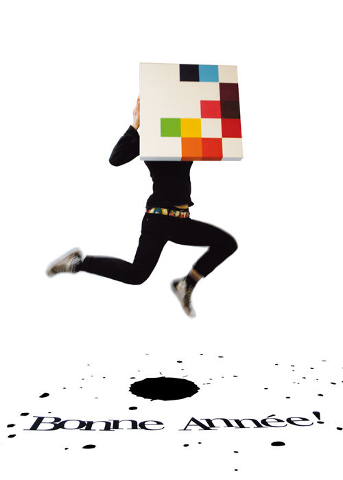 A person jumps while holding a pixelated artwork covering their face. The phrase "Bonne Année!" is written on the ground in large text.