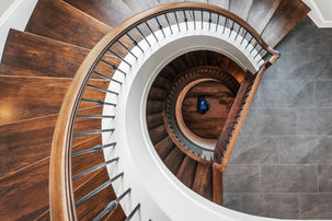 Overhead view of a custom spiral staircase with dark wood steps, black iron balusters, and a white railing, showcasing a luxury home 2019s modern architectural design.