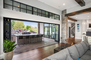 Luxurious indoor-outdoor living space with a retractable glass wall, an outdoor kitchen with bar seating, and modern interior design, including wood floors and stone accents.