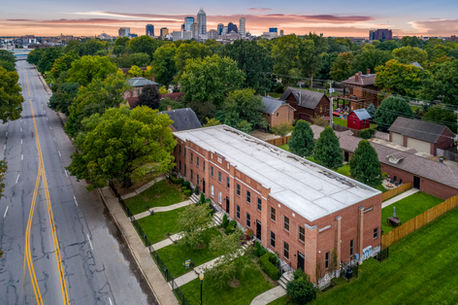 Aerial view of a red-brick townhome complex in Indianapolis with lush green lawns and the downtown skyline in the background, highlighting urban real estate and investment potential.