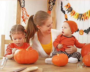 Woman with two young children, surrounded by pumpkins, in a Halloween-themed room with orange and black decorations, smiling and engaged.