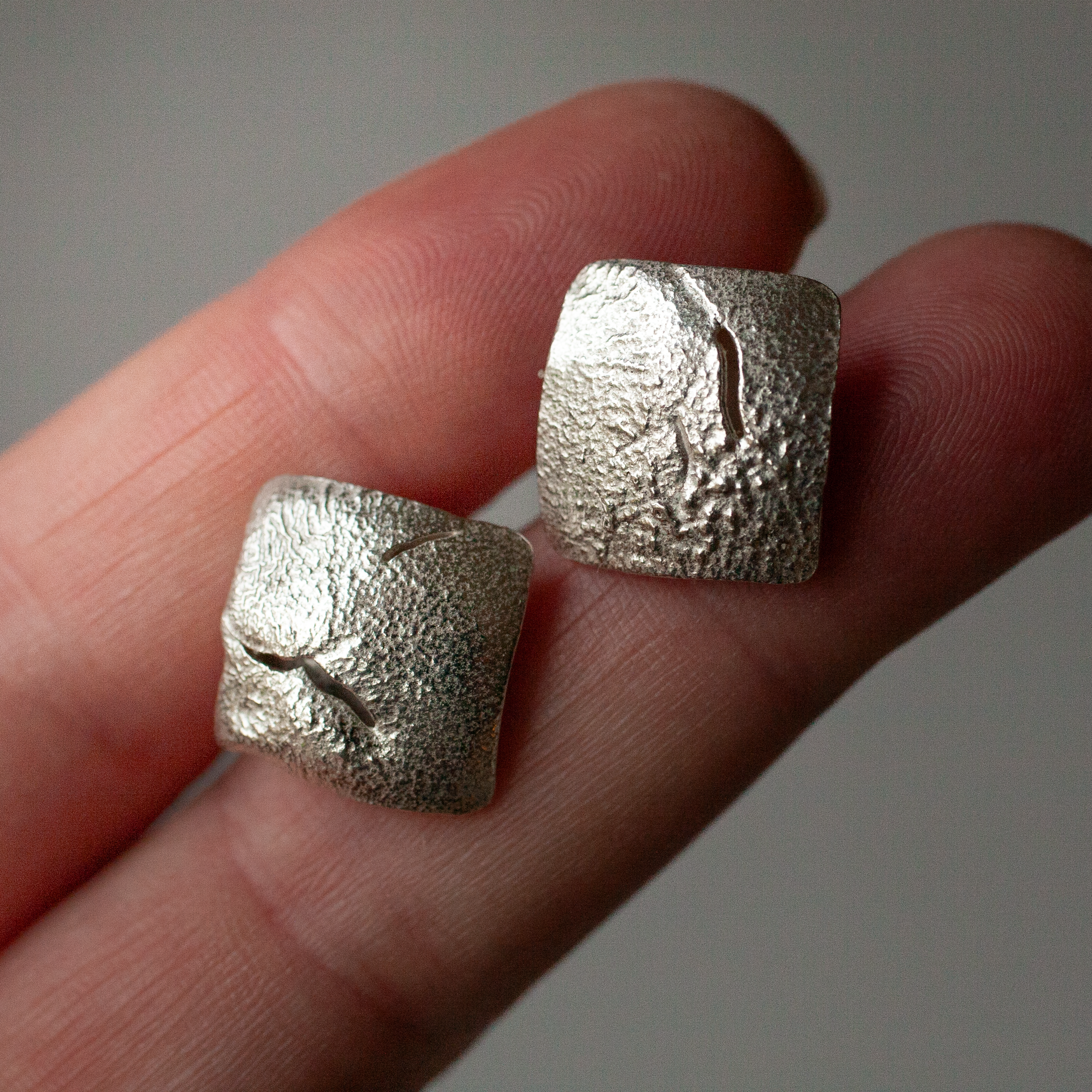 Fingers holding pair of handcrafted square silver studs