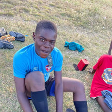 A player in Zambia ties his cleats, wearing a donated Oakville Soccer Club jersey (2022).