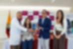 Cuatro personas posan con un premio en un evento, frente a un fondo de paneles rosas y blancos del Hospital Vozandes Quito. Sonrientes.