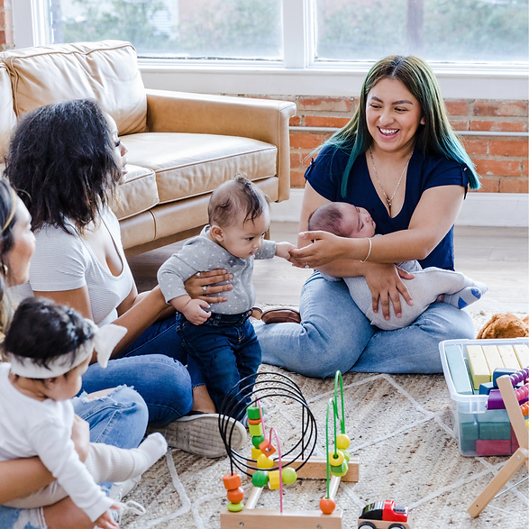 Three mothers sitting on the floor with their babies in their laps. There are toys on the floor in front of the babies
