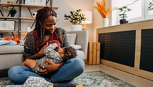 A mother sitting on the floor crossed legged breastfeeding her baby.