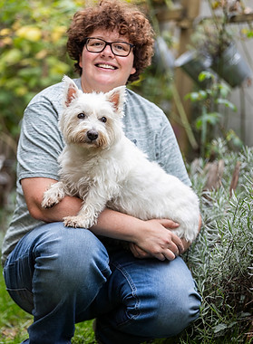 Sabine Miebeck is sitting next to a lavender. Her West-Highland-White-Terrier Maja is sitting on her lap.