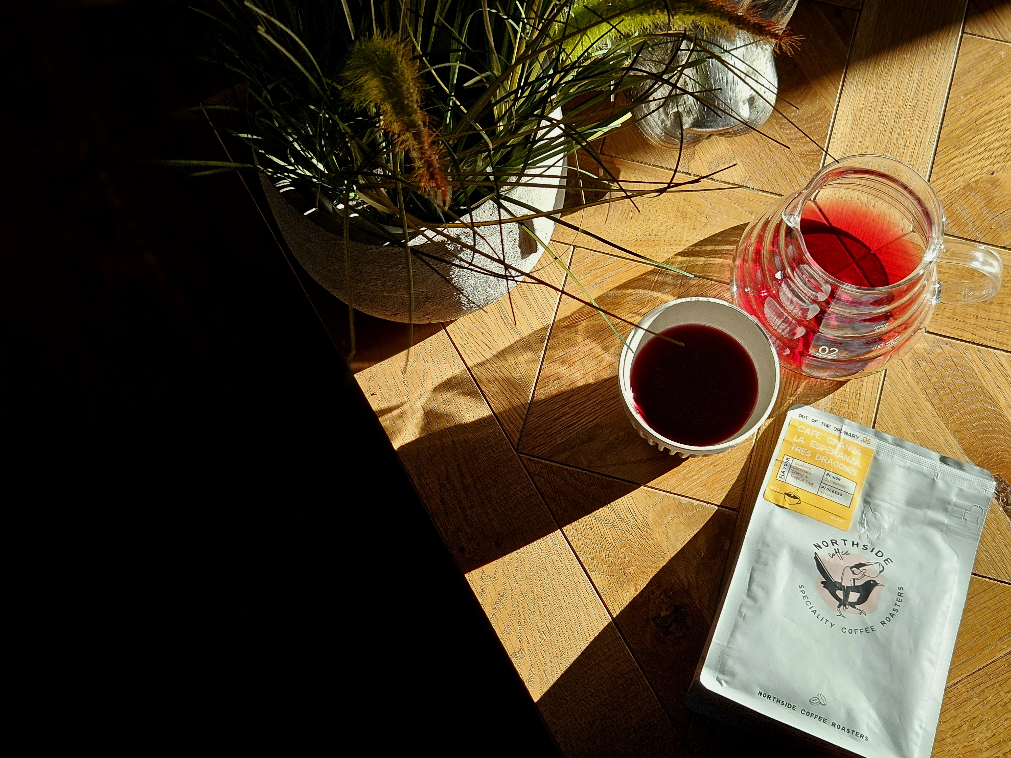 Northside coffee bag, a cup of filter coffee and a glass coffee jug on a sunlit wooden table