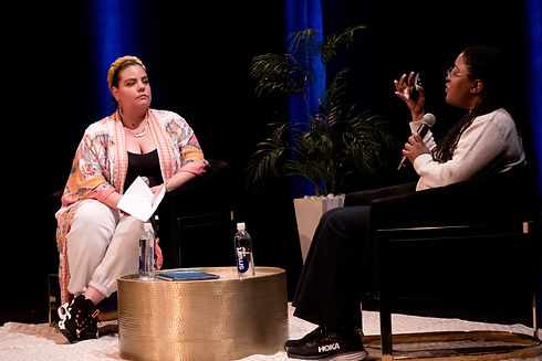 Dalia speaking on stage with mic in their hand.