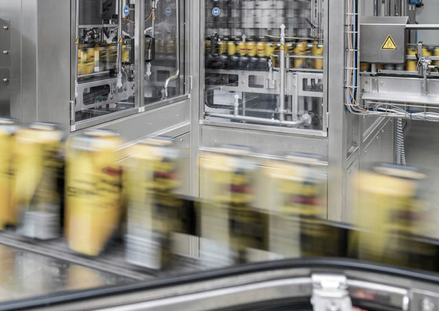 Eine laufende Abfüllanlage für Getränkedosen, auf der gelbe Dosen in Bewegungsunschärfe am Betrachter vorbeirasen