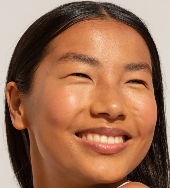 A smiling woman with glowing, clear skin, looking to the side with a bright expression.