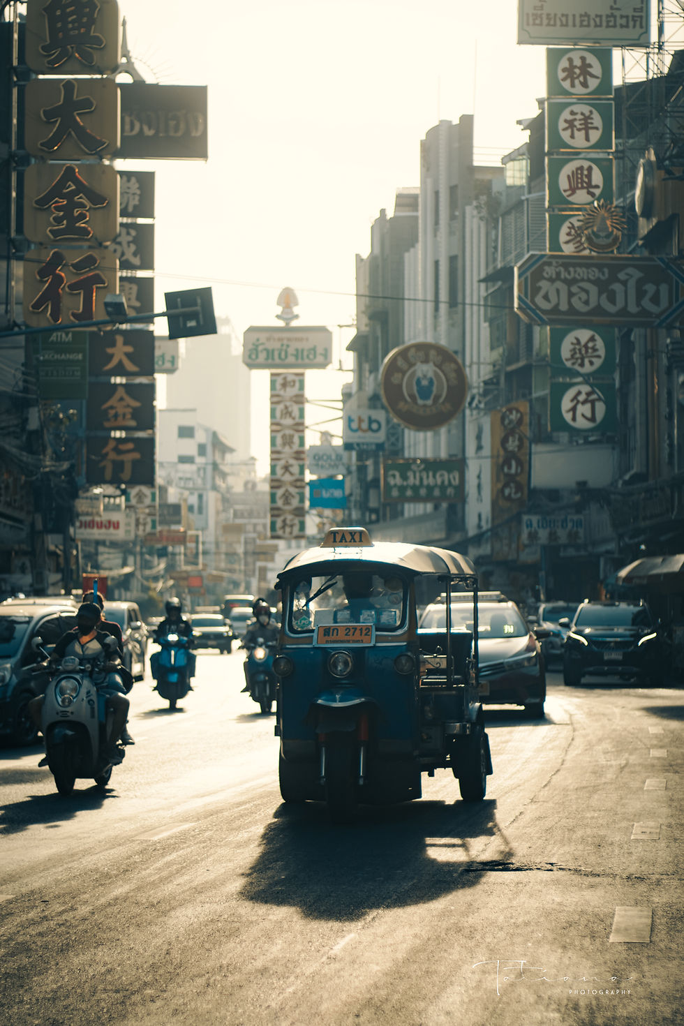 Silhouetted tuk-tuk driving into the distance in hazy Chinatown Bangkok at sunrise
