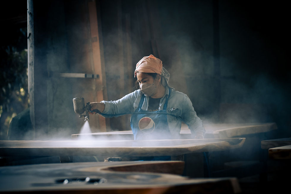 Female artisan spraying varnish in haze-filled woodworking shop in Ban Tawai Chiang Mai.