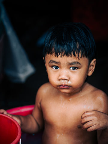 hirtless Thai boy holding a red basin, captured with droplets on his chest and a serious gaze.