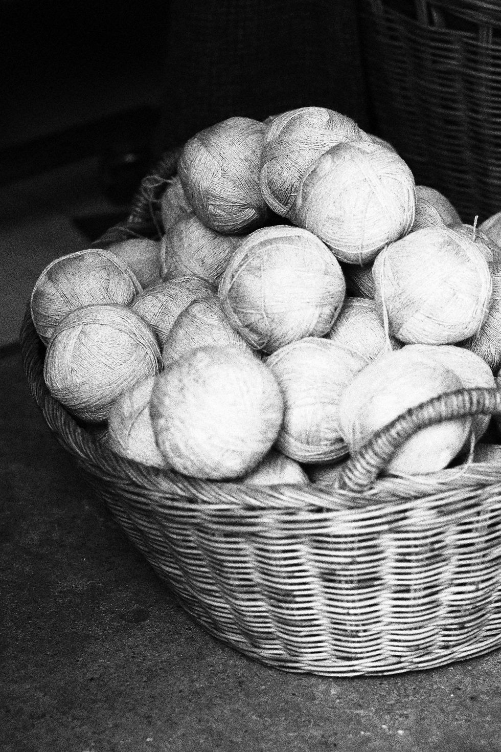 Black and white image of a wicker basket filled with round balls of yarn or twine on a shop floor.