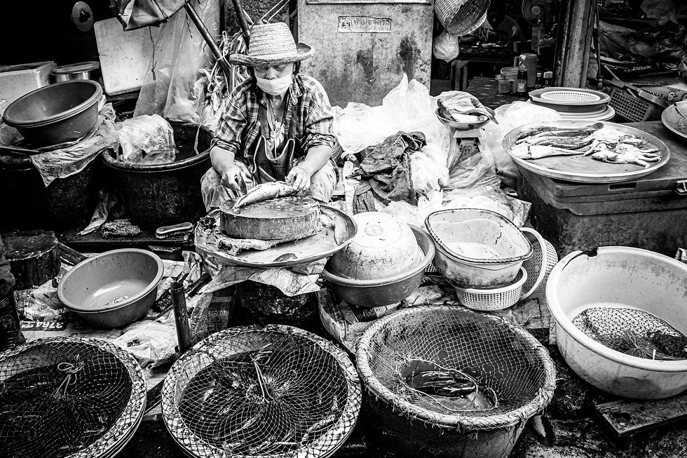 Woman preparing fish at a traditional market in Thailand, surrounded by plastic bowls and containers.