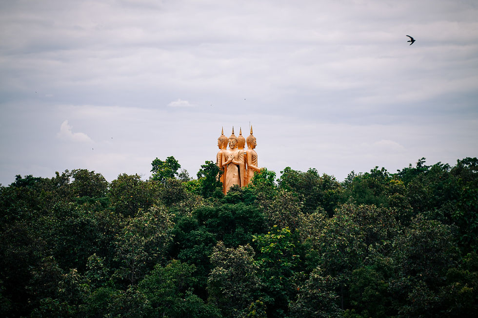 A distant view of the golden four-faced Buddha statue at Wat Doi Sapphanyu (Wat Nam Bo Tib), rising above lush green treetops under a cloudy sky — symbolizing serenity and spiritual presence in the Thai landscape.