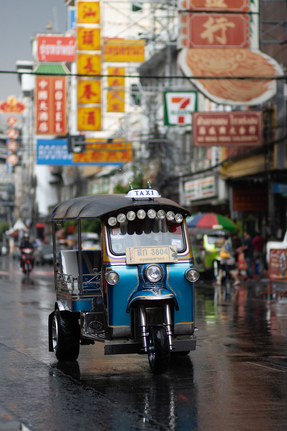 Tuk-tuk driving on wet street with colorful vertical signs in Bangkok’s Chinatown