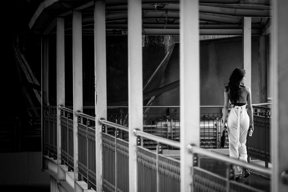 Black and white street photograph of a woman walking through a modern pedestrian bridge, framed by vertical architectural lines.