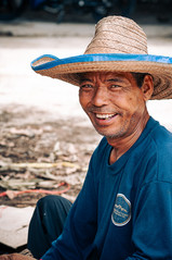Portrait of a Thai woodworker wearing a straw hat, smiling warmly at the camera in Ban Tawai, Chiang Mai.