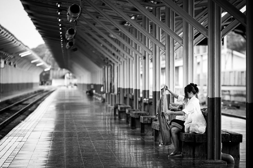 Black and white portrait of a woman in profile waiting by train tracks, captured in Chiang Mai.