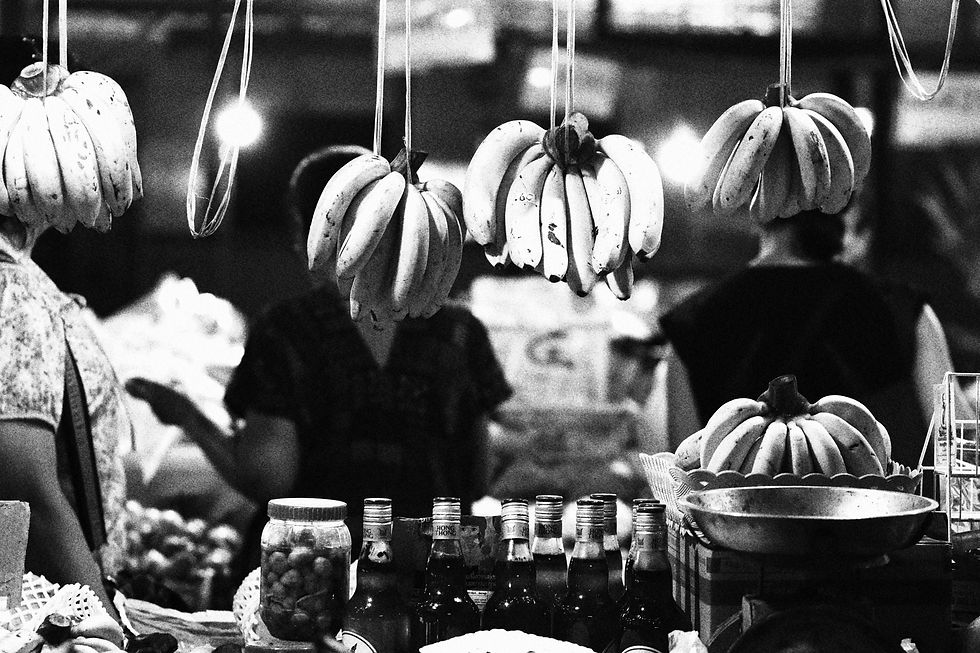 Close black and white view of banana clusters suspended over jars and bottles at a busy market stall.