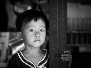 Black and white portrait of a young boy holding a pillar, with half his face in shadow, conveying introspection and quiet strength.
