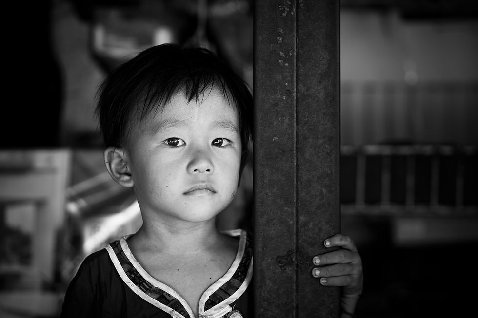 Black and white portrait of a young boy holding a pillar, with half his face in shadow, conveying introspection and quiet strength.