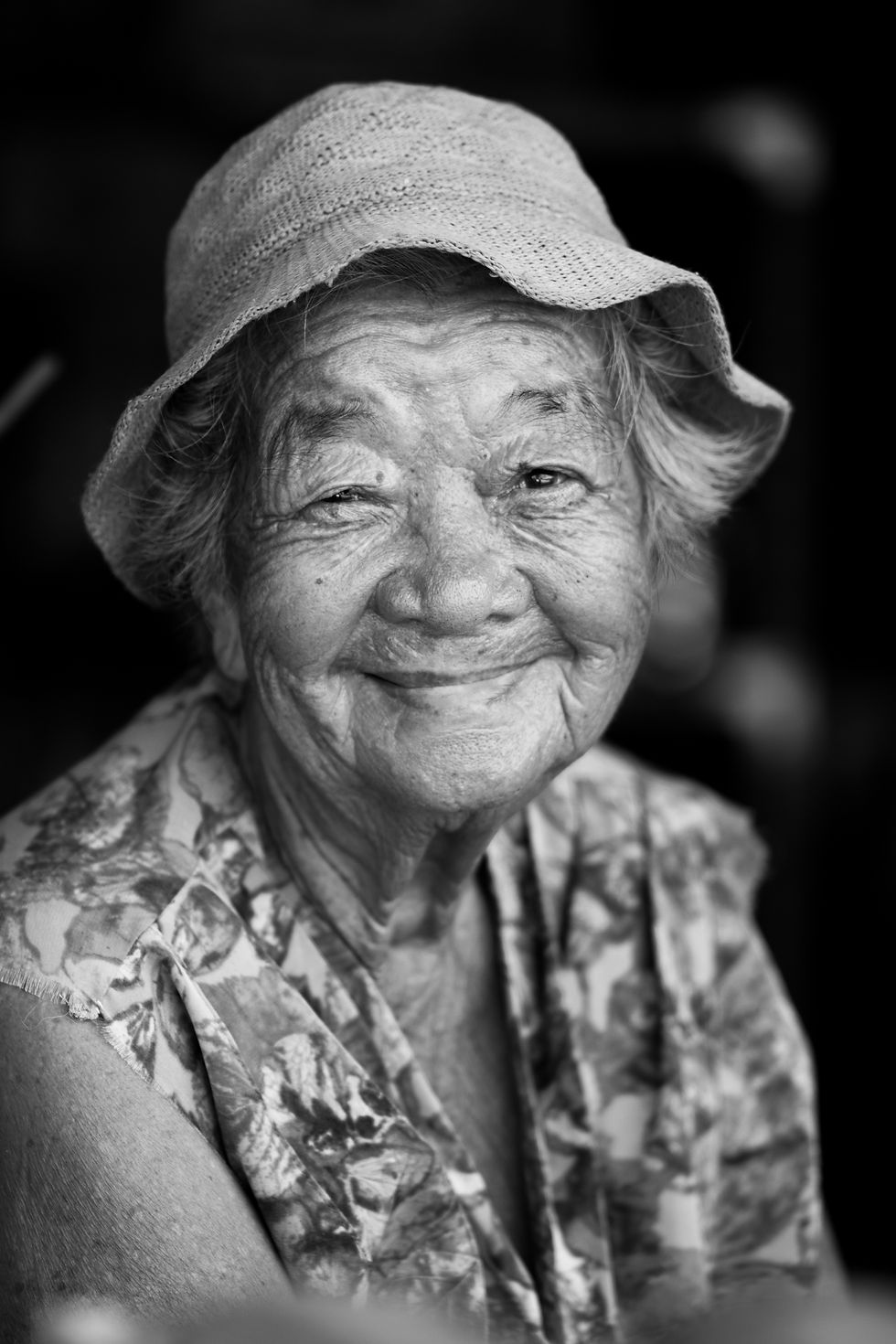 Elderly woman smiling warmly in natural light, wearing a sunhat.
